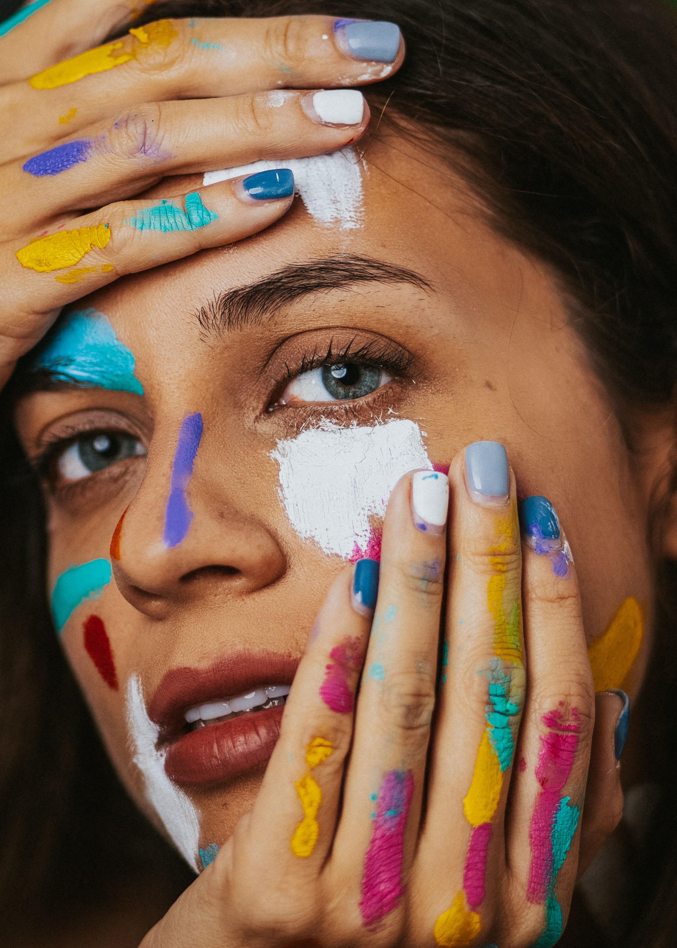 Woman's face with hands on her cheek and forehead covered in colored paint