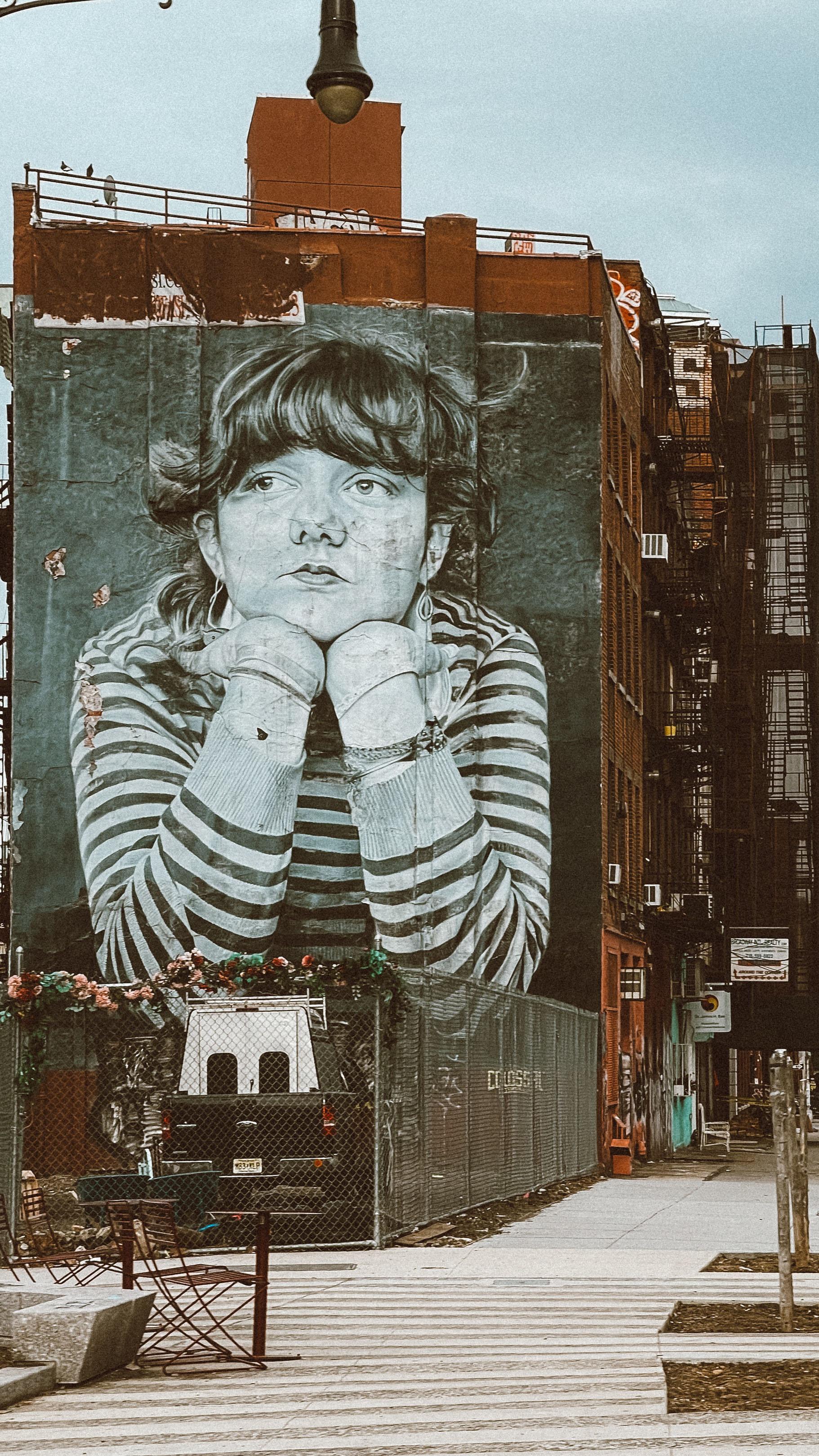 A girl with her chin resting on her fists painted on the side of a brick building